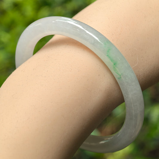 Natural Grade-A icy glutinous light white jadeite round-bar bangle with faint green accent shown on wrist, highlighting smooth translucent surface.
