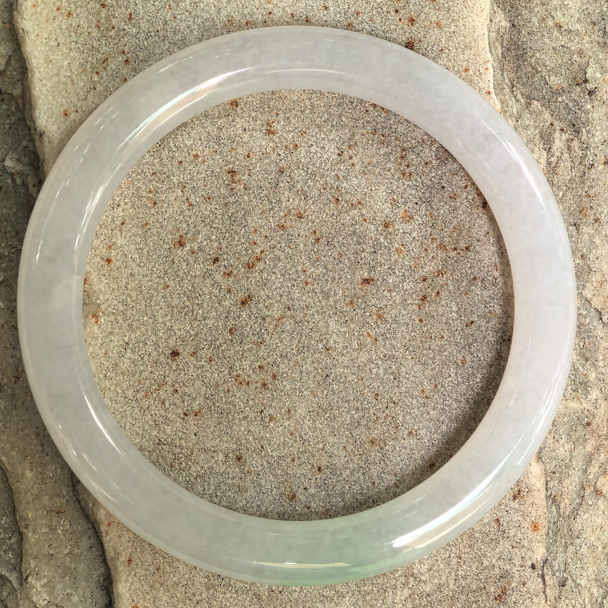 Natural jadeite bangle displayed on stone surface showing round-bar shape and polished finish.
