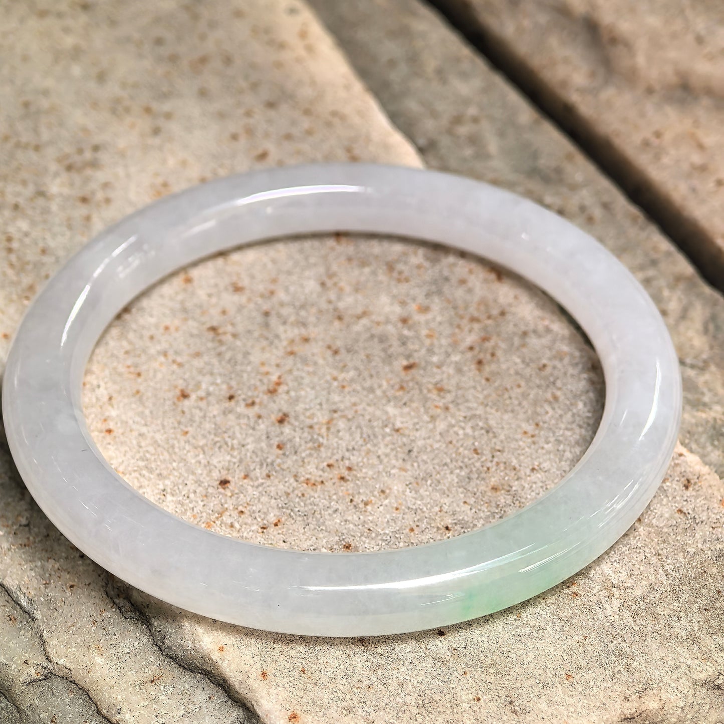 Jadeite bangle photographed at different angle emphasizing circular form, translucency, and surface structure.