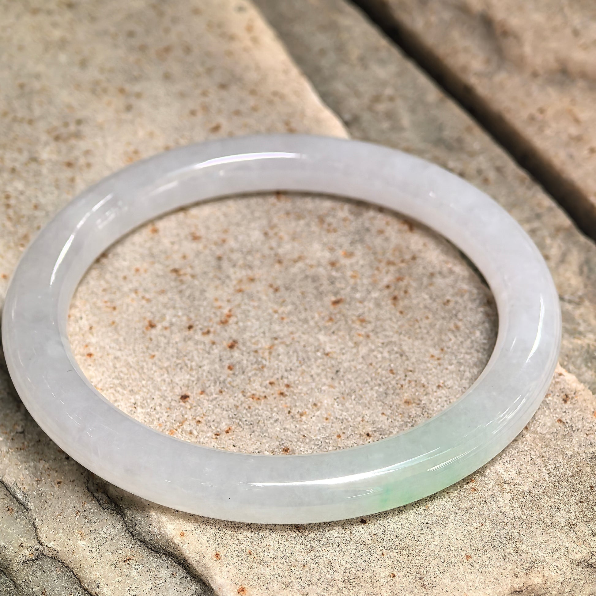 Jadeite bangle photographed at different angle emphasizing circular form, translucency, and surface structure.