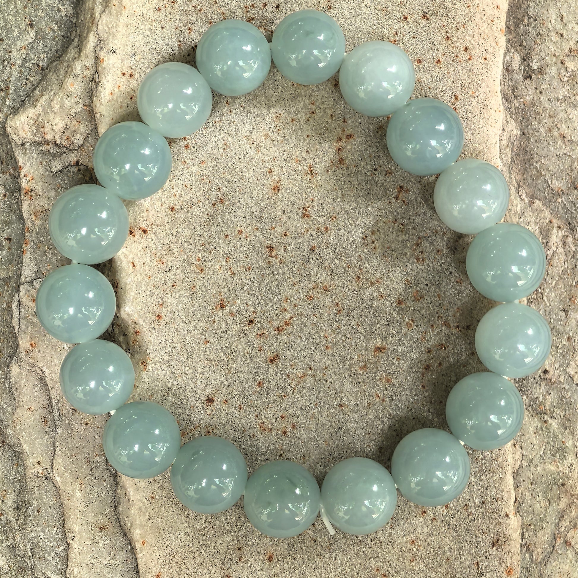 Natural green jadeite bead bracelet displayed on stone background.