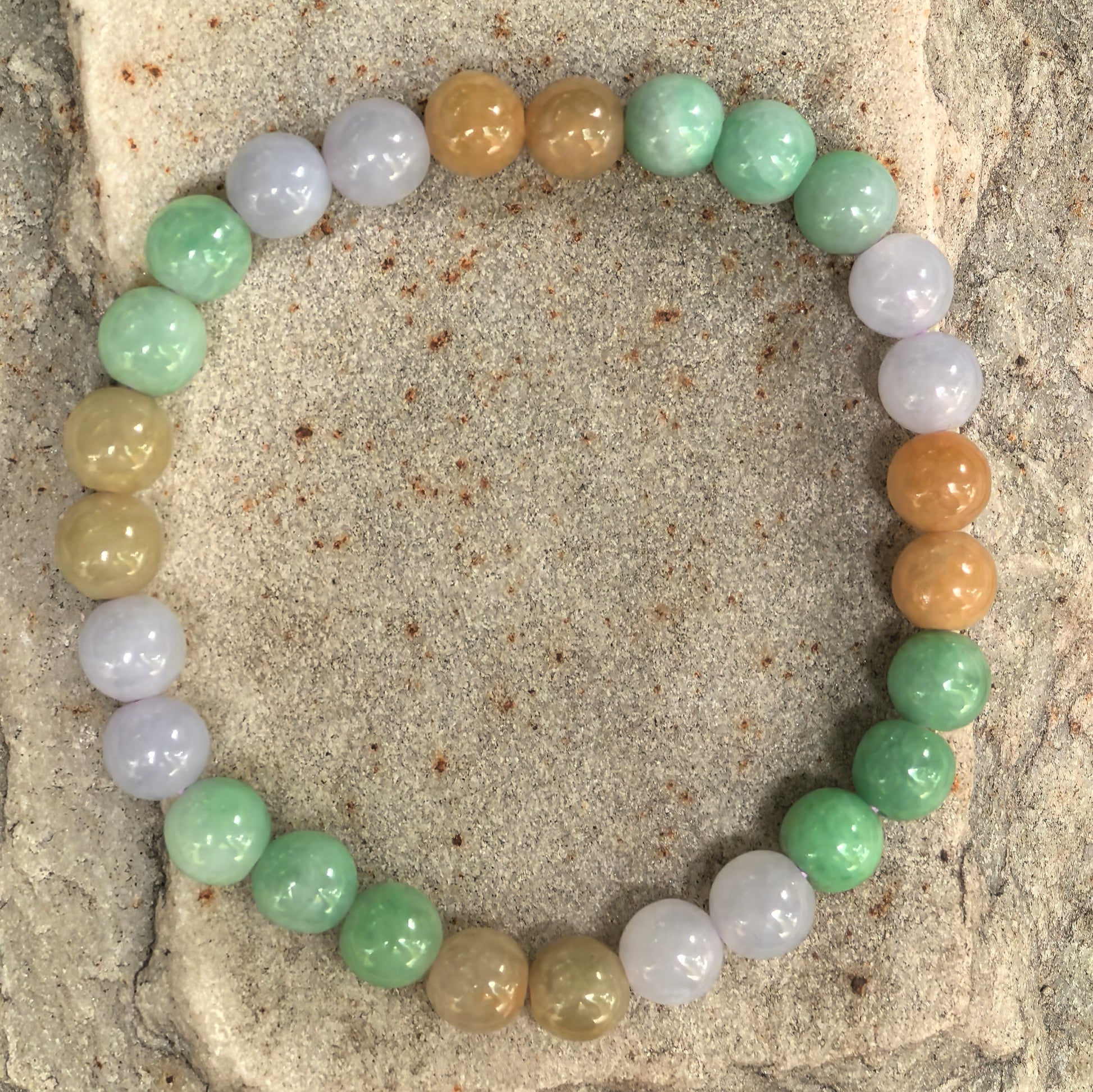 Natural jadeite bead bracelet displayed on stone background showing soft mixed colors.