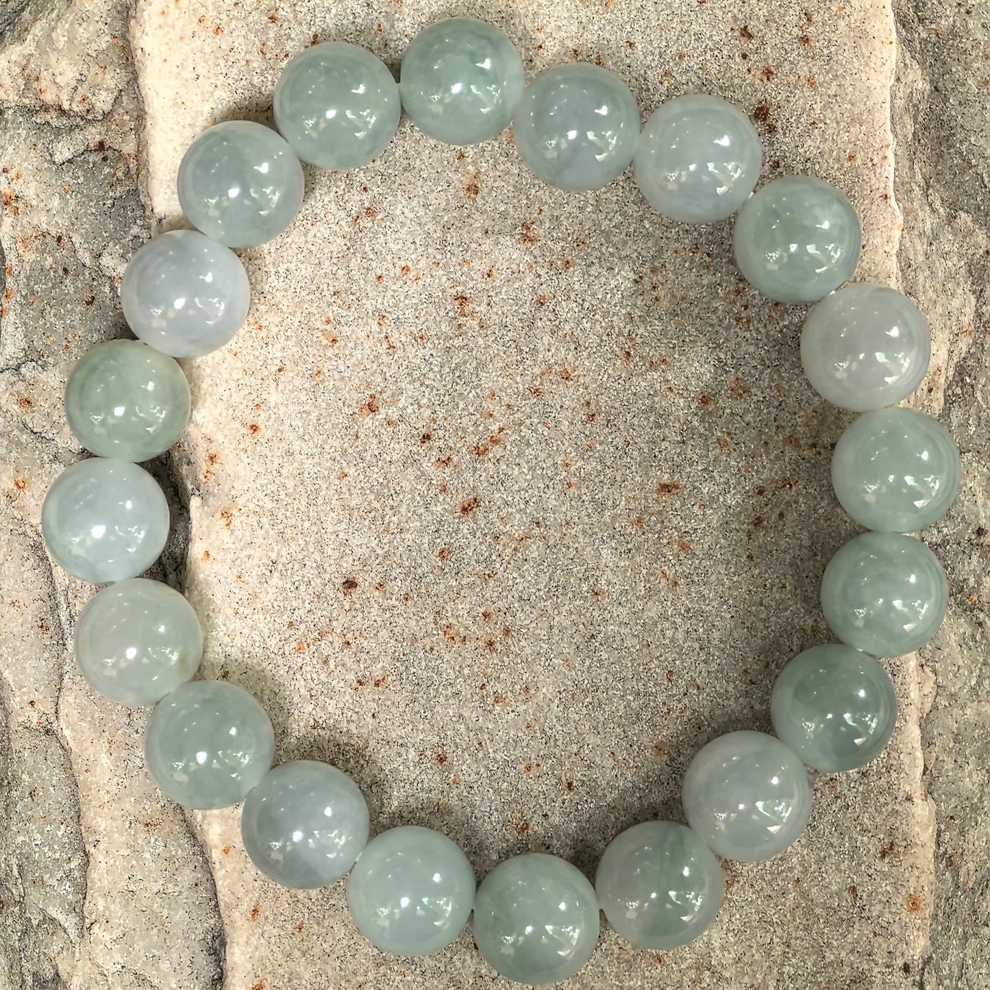 Pale green jadeite bead bracelet displayed on stone background.