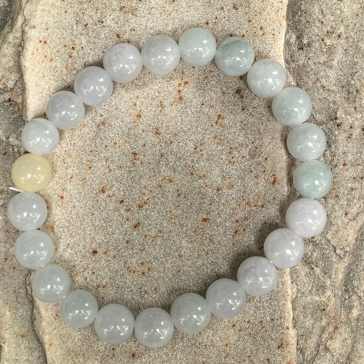 Glutinous pale green jadeite bead bracelet displayed on stone background.