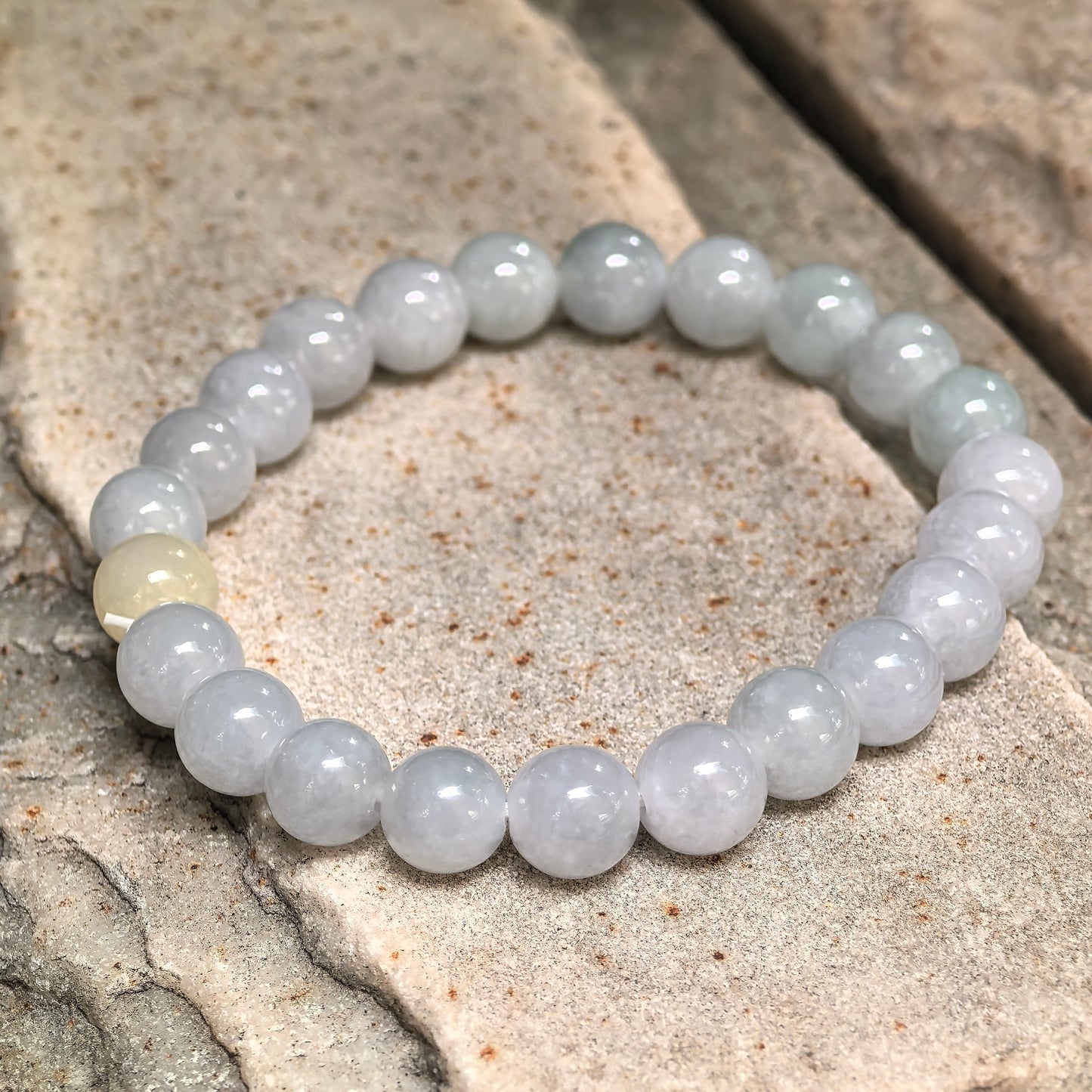Natural jadeite bead bracelet showing subtle pale green and light warm yellow variation.