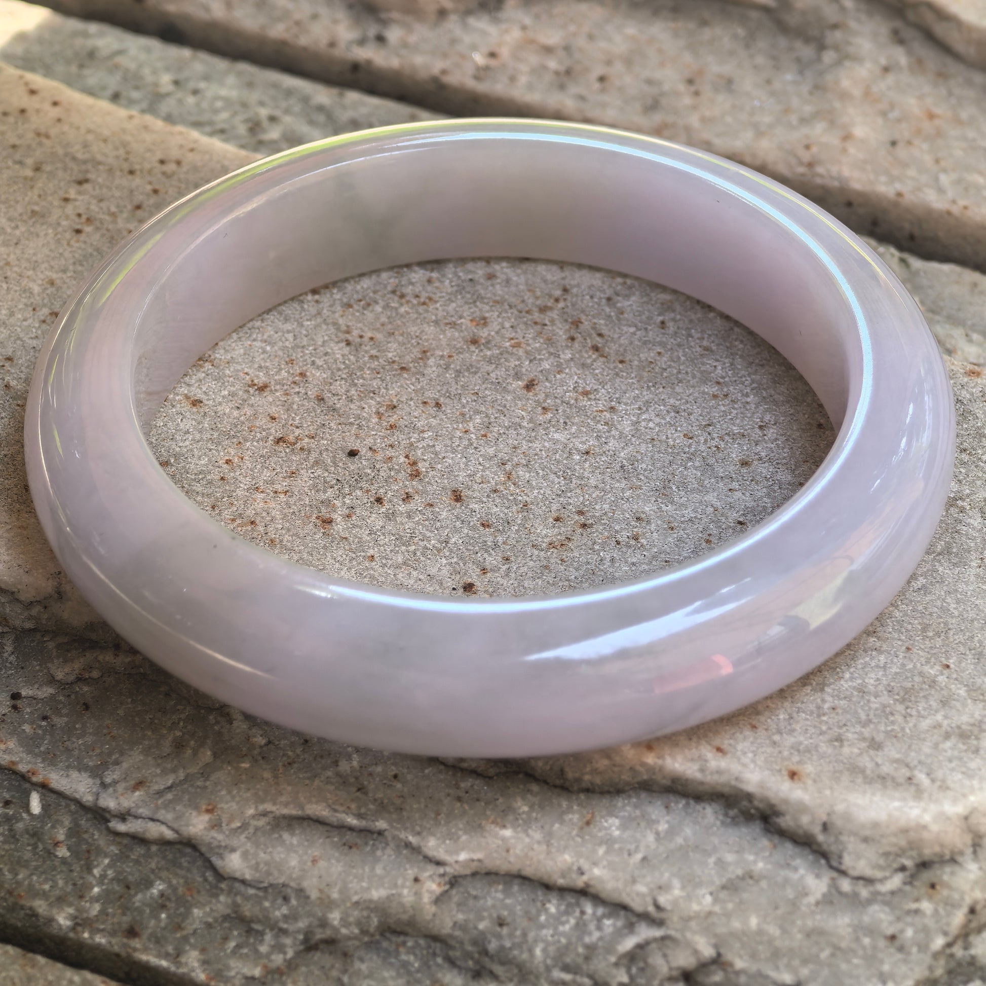 Angled view of a D-shape jadeite bangle with glutinous texture and no cracks.
