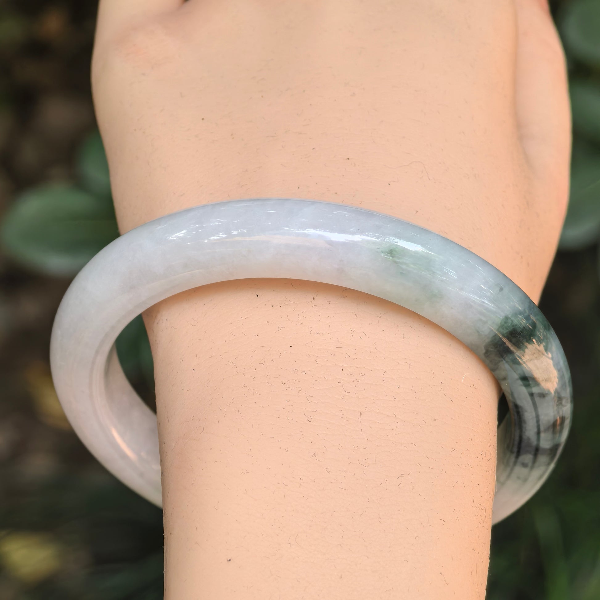 Close-up of a pale green jadeite bangle with deep green floating flower patterns.
