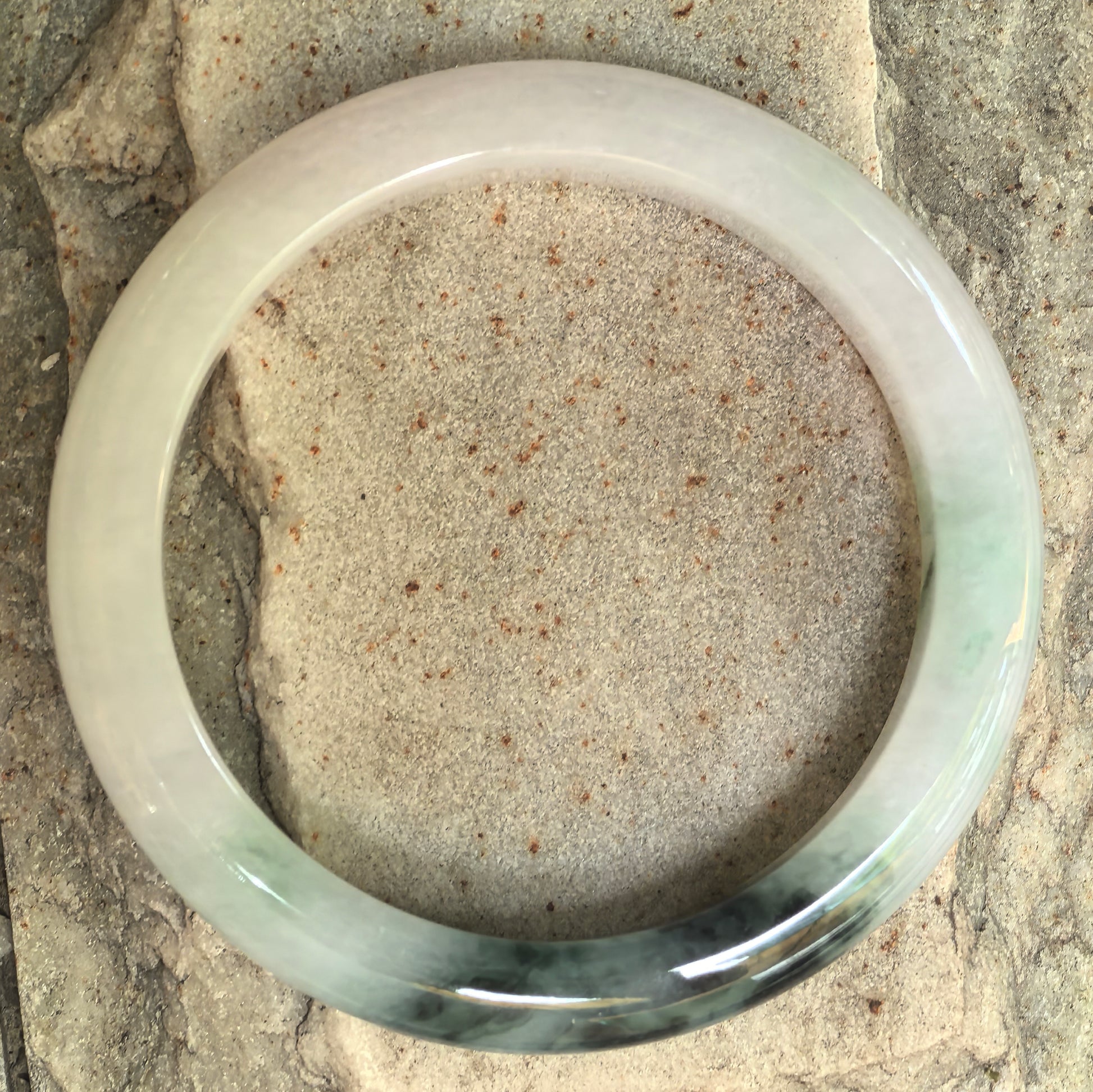Top view of a D-shape jadeite bangle showing pale green base and dark green floating flowers.
