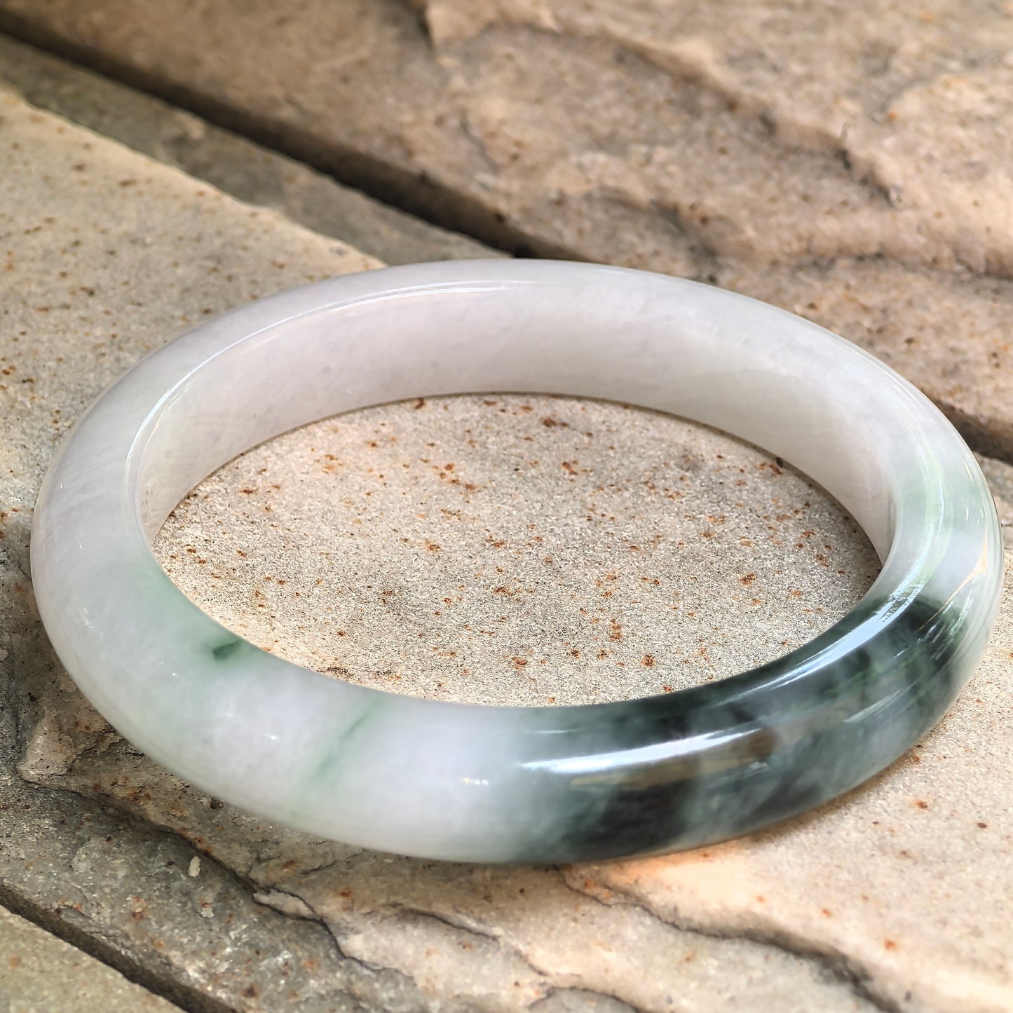 Angled view of a glutinous green jadeite bangle with smooth polished surface.
