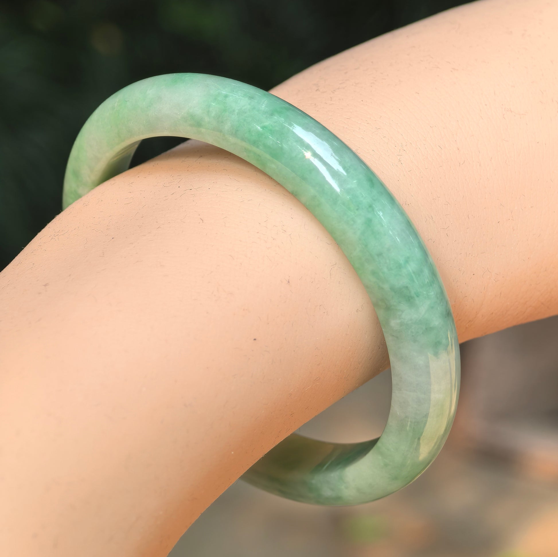 Natural Grade-A glutinous green slim D-shape jadeite bangle worn on the wrist.
