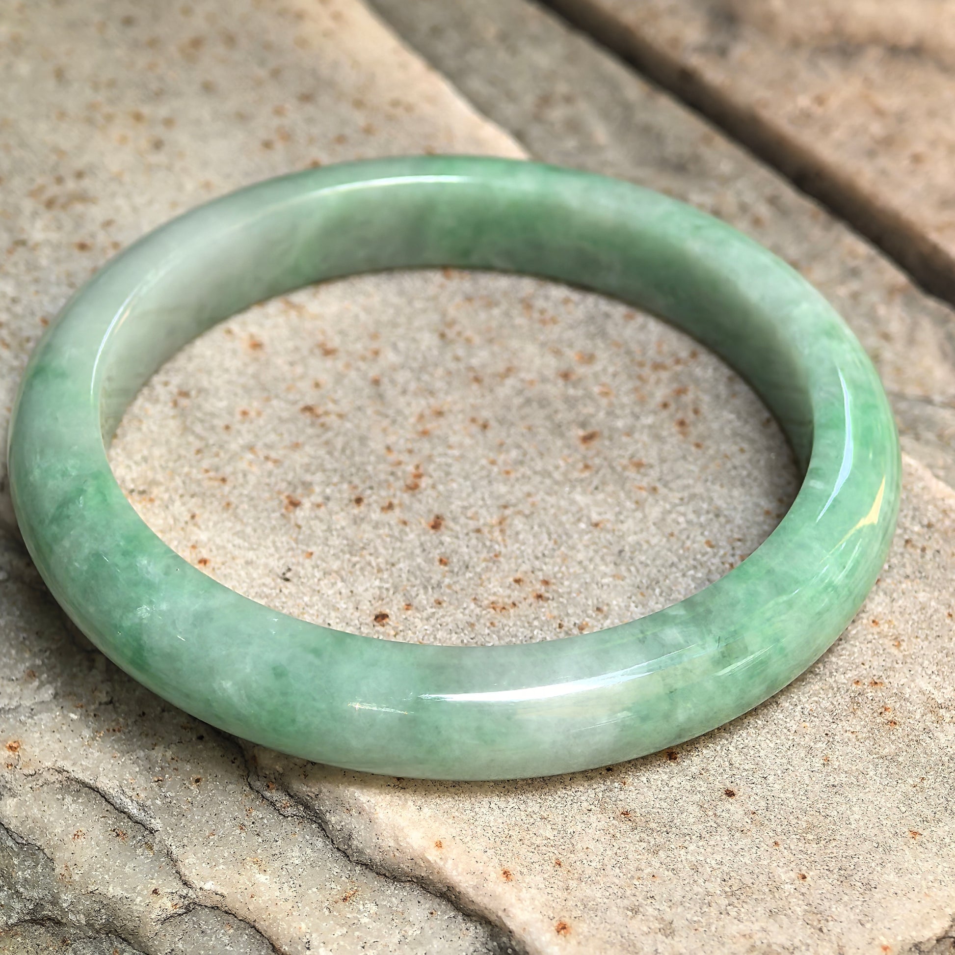 Angled view of a D-shape jadeite bangle with glutinous texture and fresh green tone.
