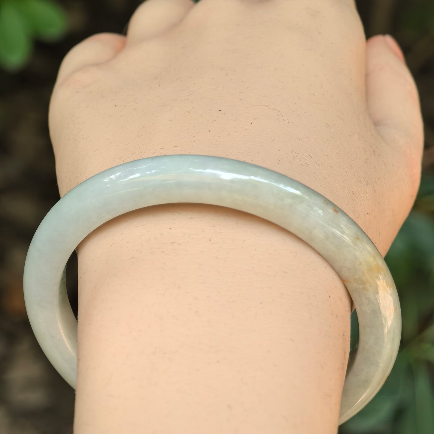 Close-up of a white jadeite bangle with orange scattered-gold accents and smooth luster.
