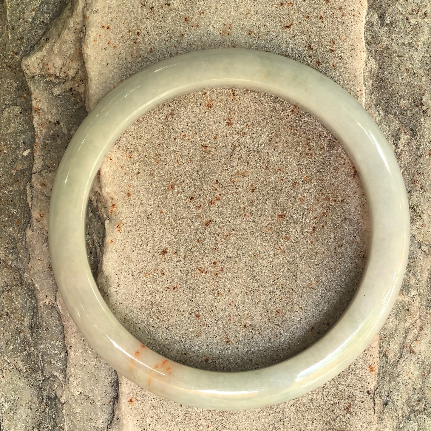 Top view of a slim pale jadeite bangle with subtle orange scattered-gold details.
