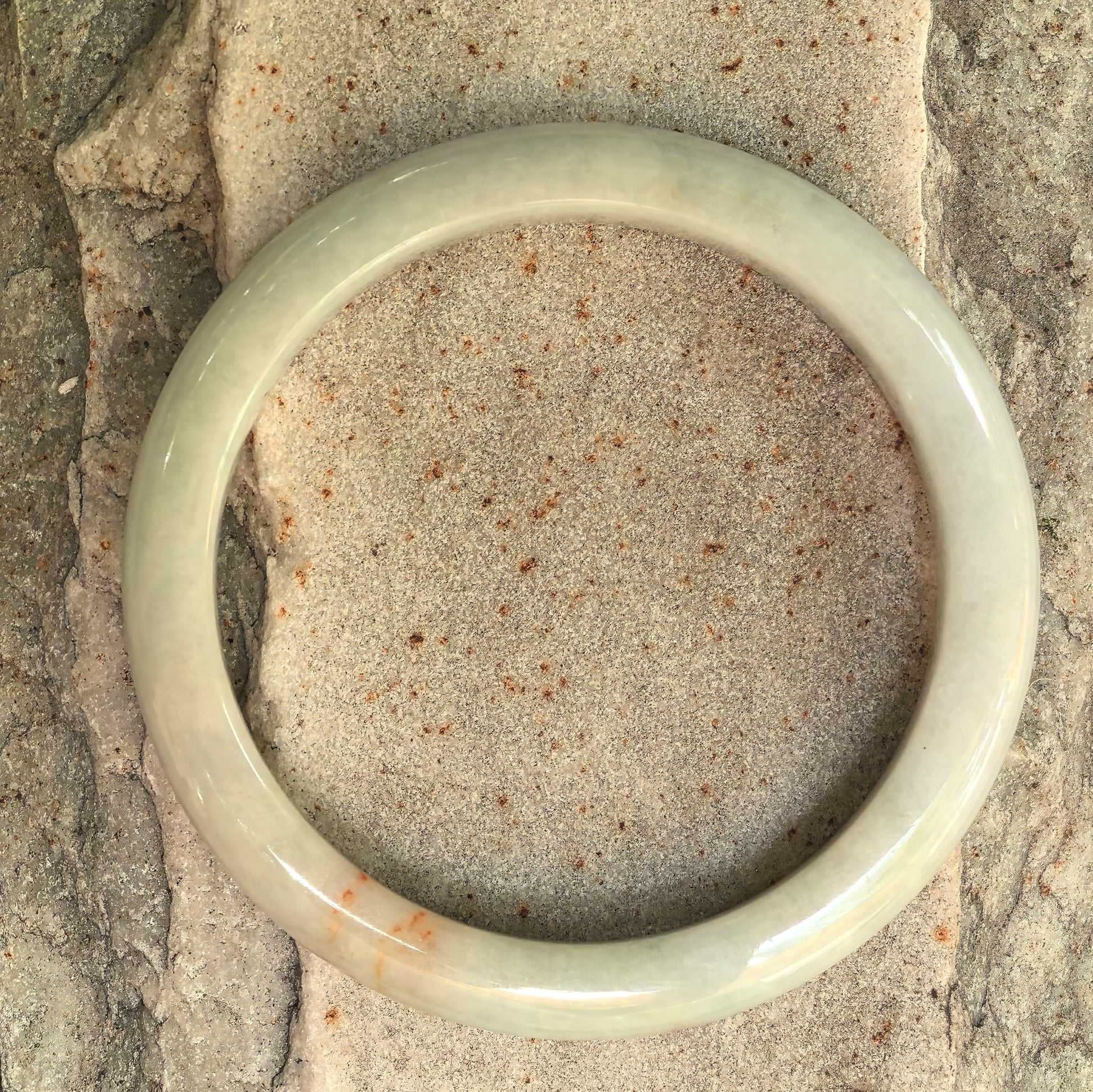 Top view of a slim pale jadeite bangle with subtle orange scattered-gold details.
