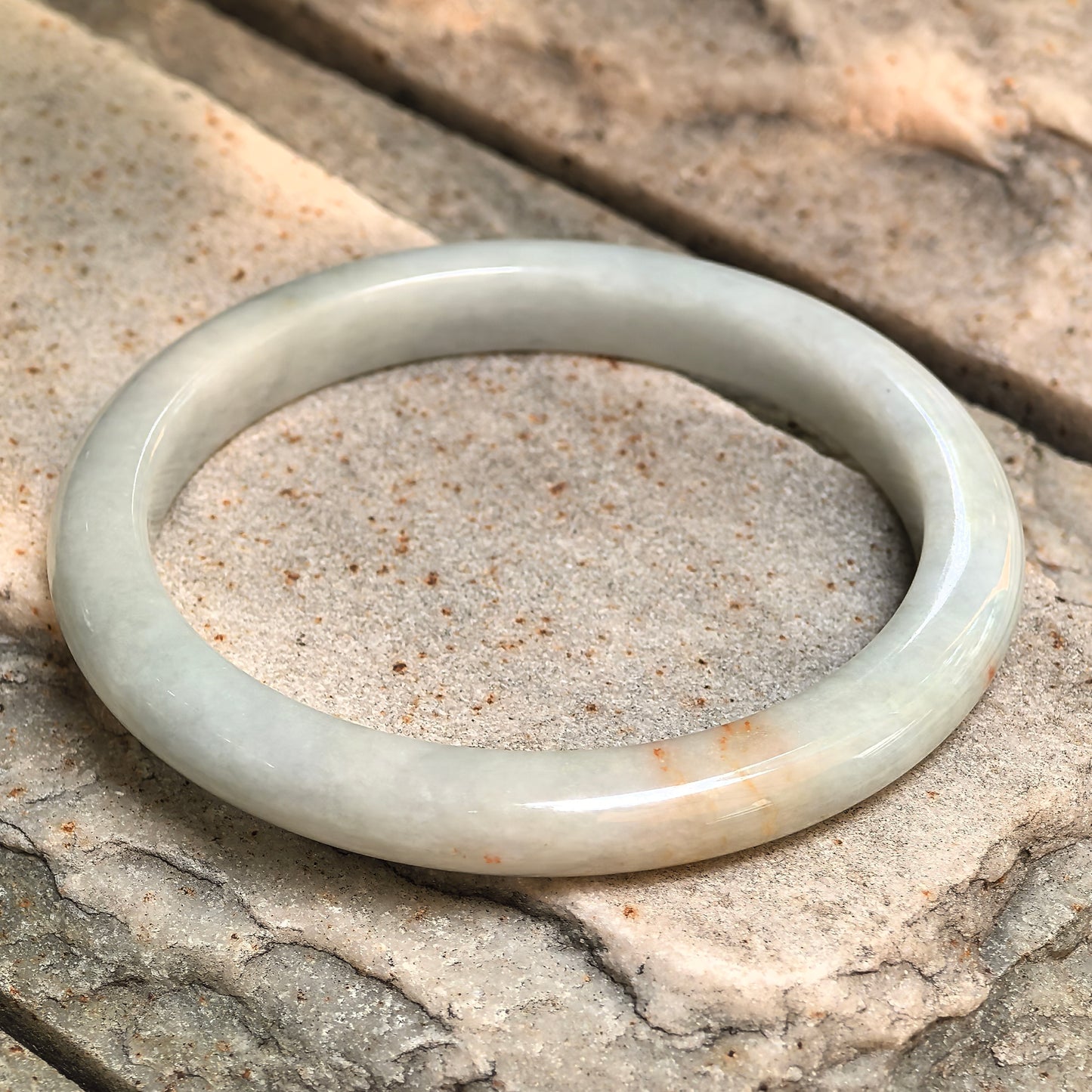 Angled view of a D-shape jadeite bangle with glutinous texture and polished surface.
