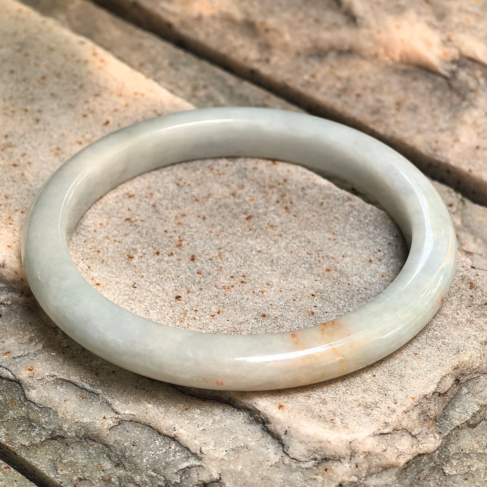 Angled view of a D-shape jadeite bangle with glutinous texture and polished surface.

