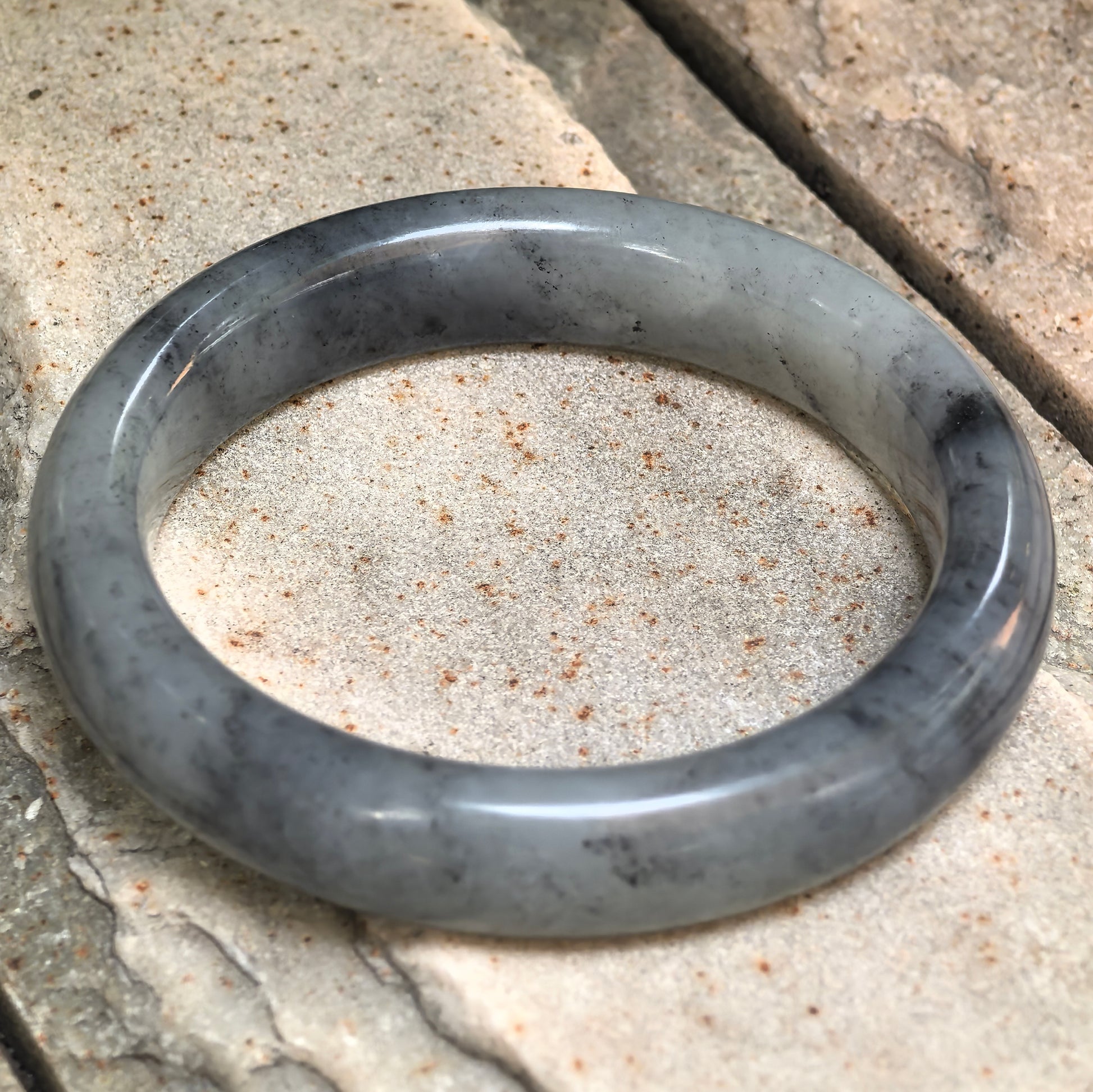 Angled view of a D-shape Hetian jade bangle with calm grey-black tone.
