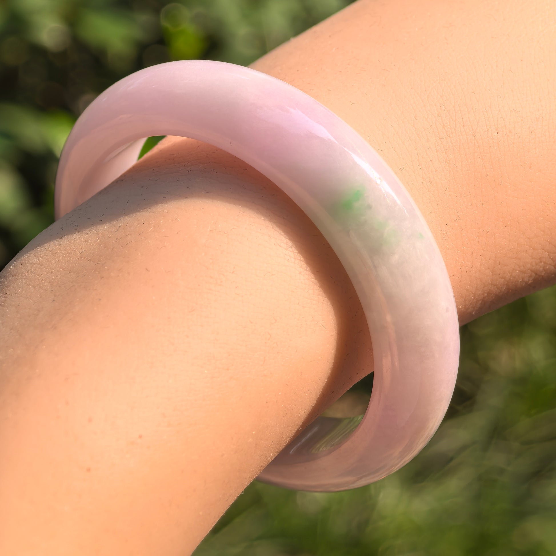 Angled view of the jadeite oval bangle under sunlight showing glutinous texture and glossy surface.
