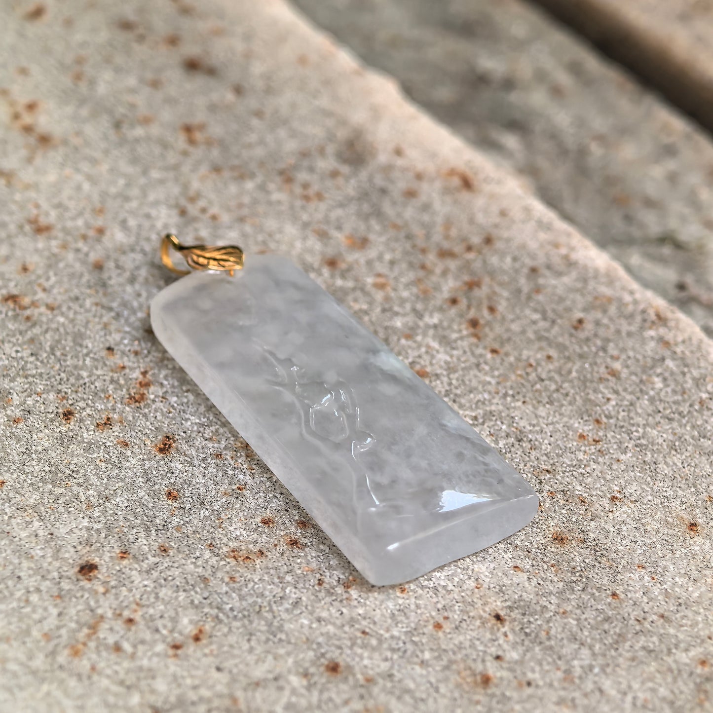Angled view of a natural icy jadeite pendant with 18K gold leaf-shaped bail.
