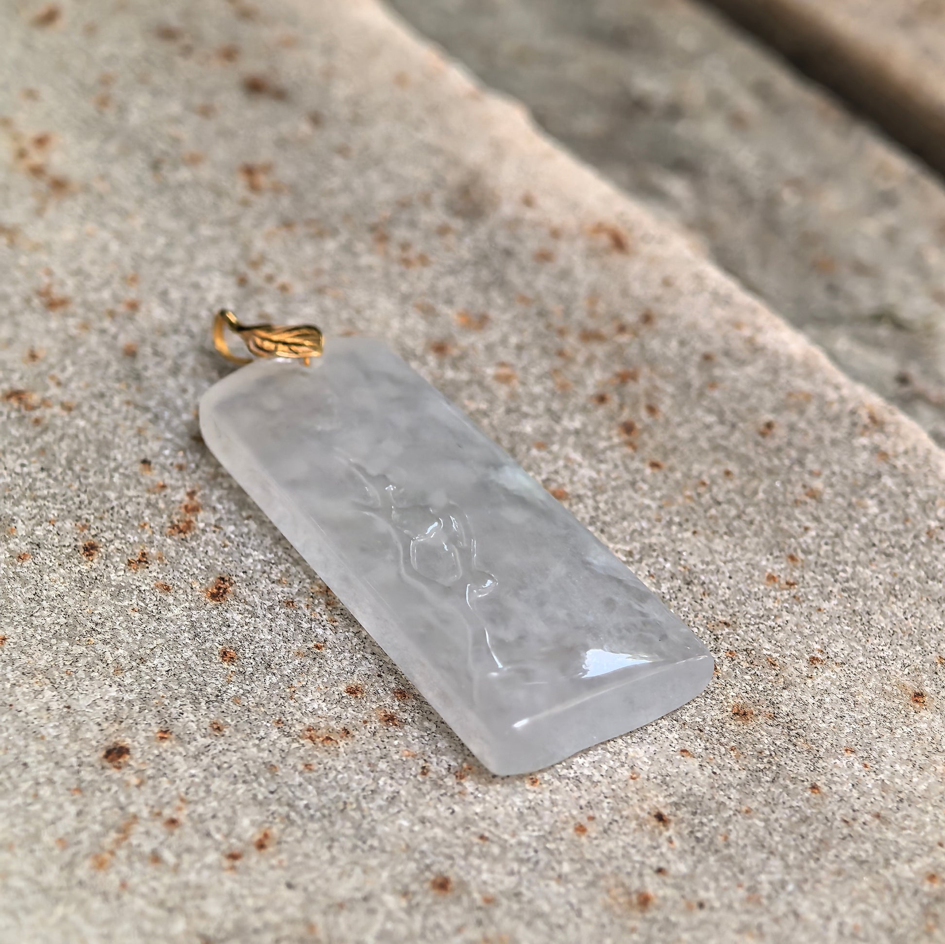 Angled view of a natural icy jadeite pendant with 18K gold leaf-shaped bail.

