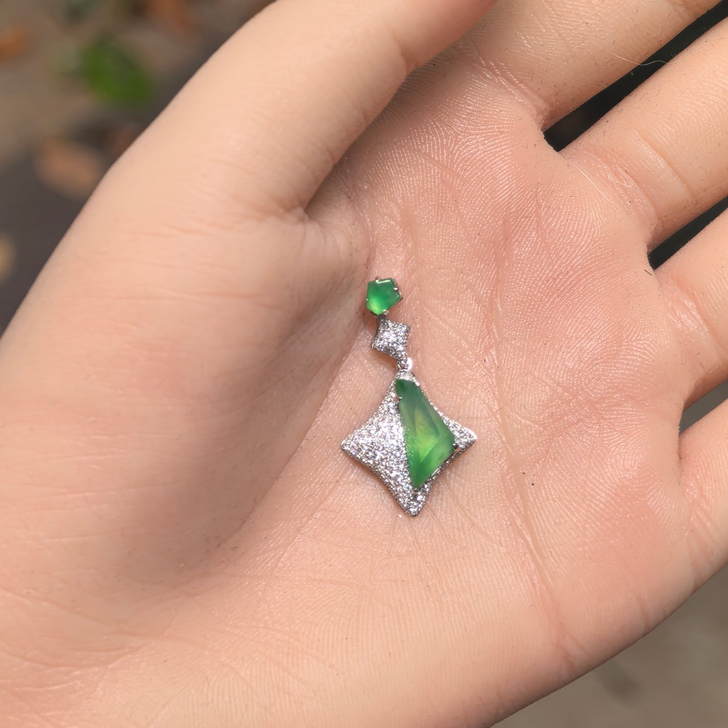 Close-up of a vivid green jadeite pendant showing luxurious geometric 18K gold setting.
