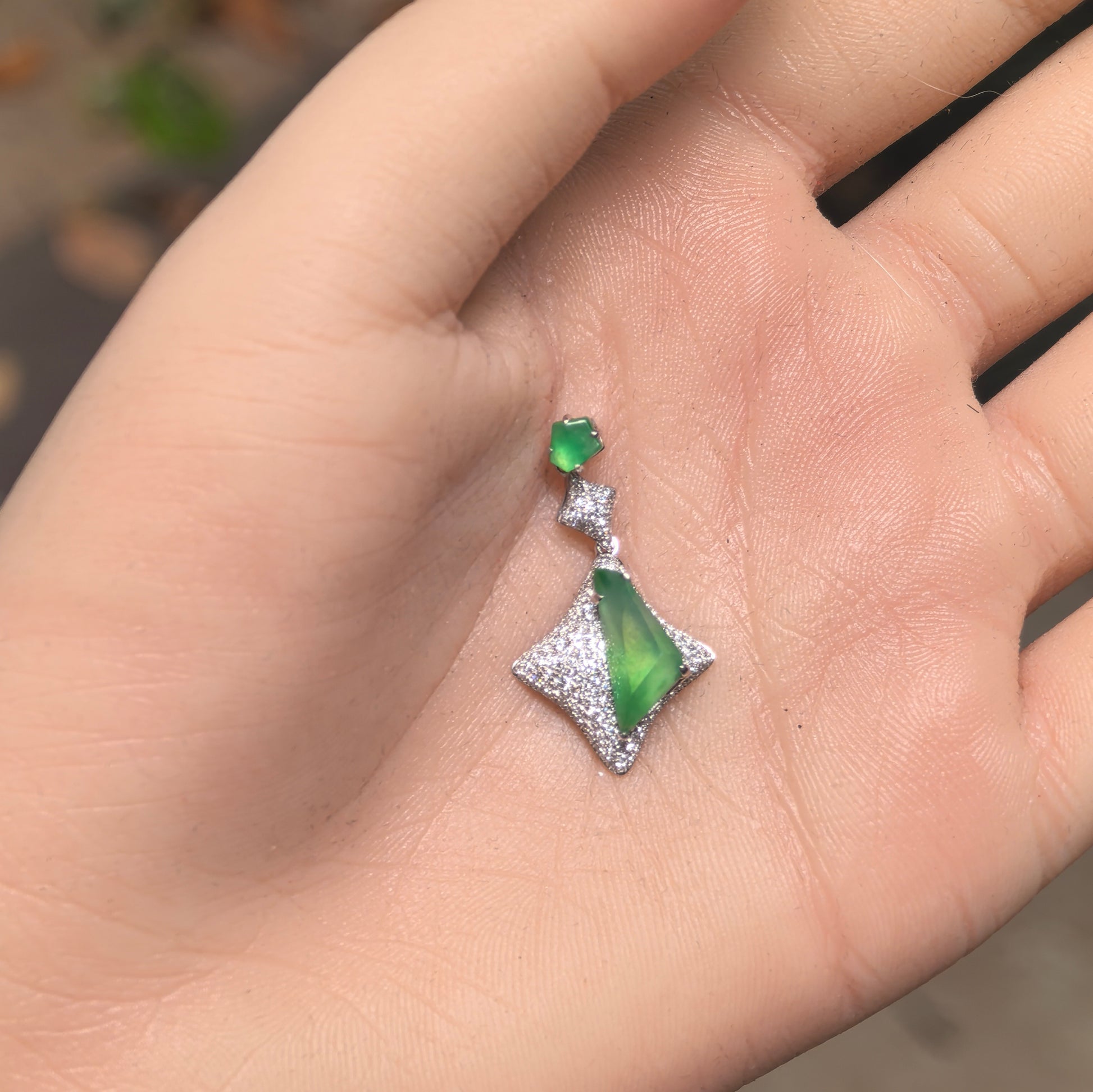Close-up of a vivid green jadeite pendant showing luxurious geometric 18K gold setting.
