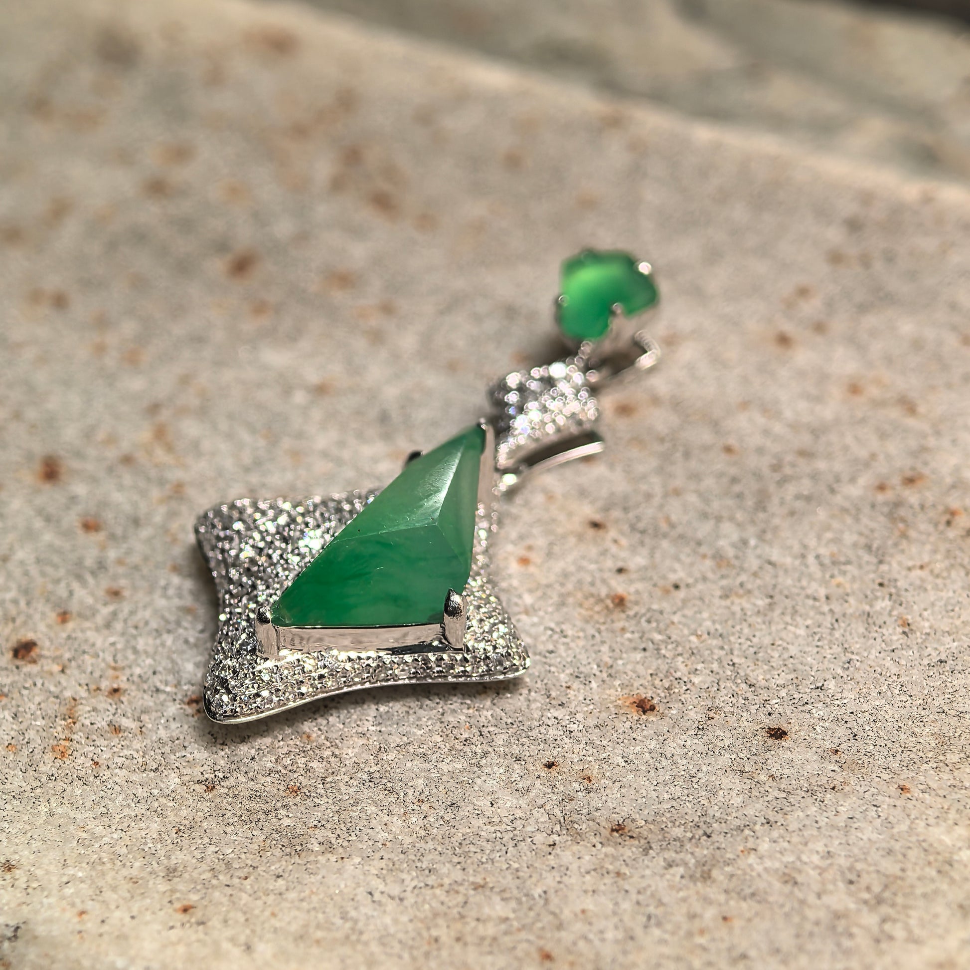 Angled view of an icy green jadeite pendant with bright color and fine jewelry setting.
