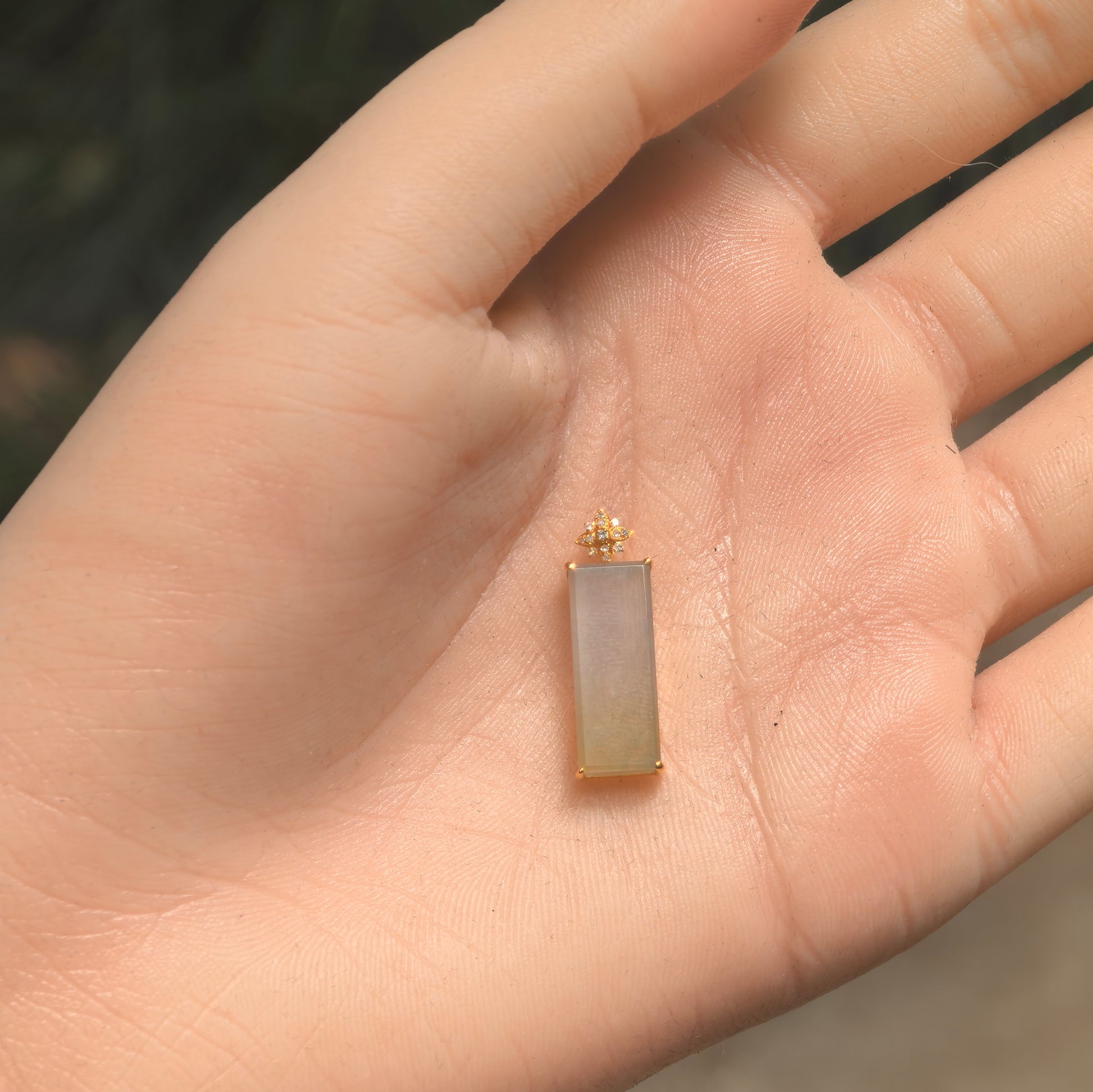Close-up of a light yellow jadeite pendant showing smooth luster and rectangular form.
