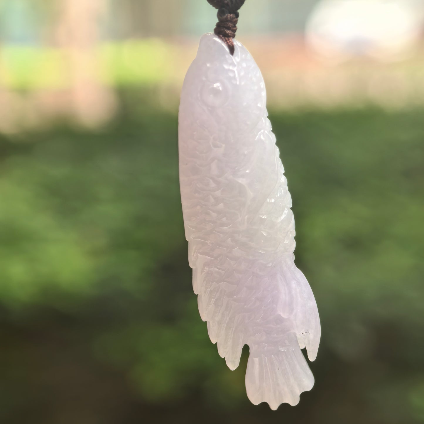 Natural Grade-A glutinous-icy light lavender fish jadeite pendant hanging in natural light.
