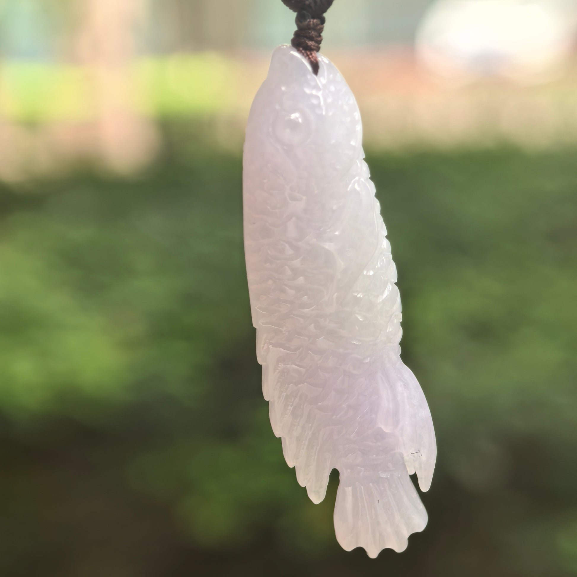 Natural Grade-A glutinous-icy light lavender fish jadeite pendant hanging in natural light.
