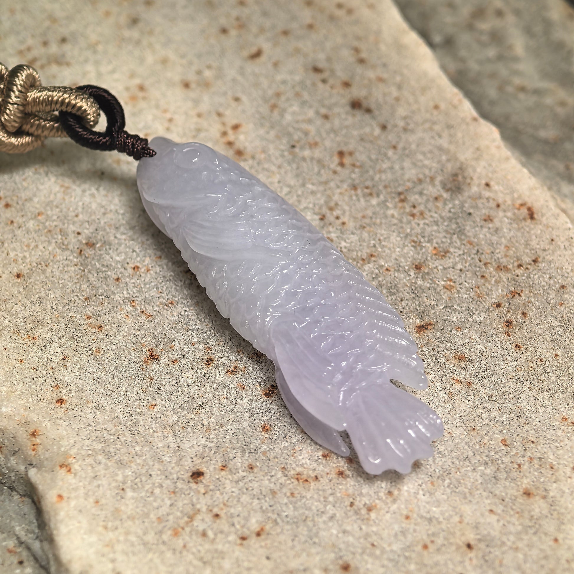 Angled view of a vivid carved fish jadeite pendant with smooth polished luster.
