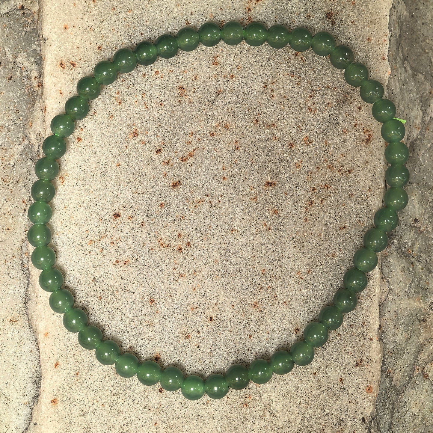 Natural green jadeite beaded bracelet arranged in a full circle on stone surface.
