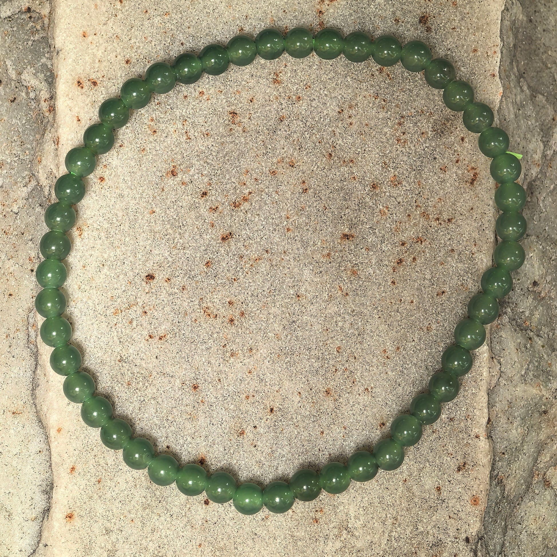 Natural green jadeite beaded bracelet arranged in a full circle on stone surface.
