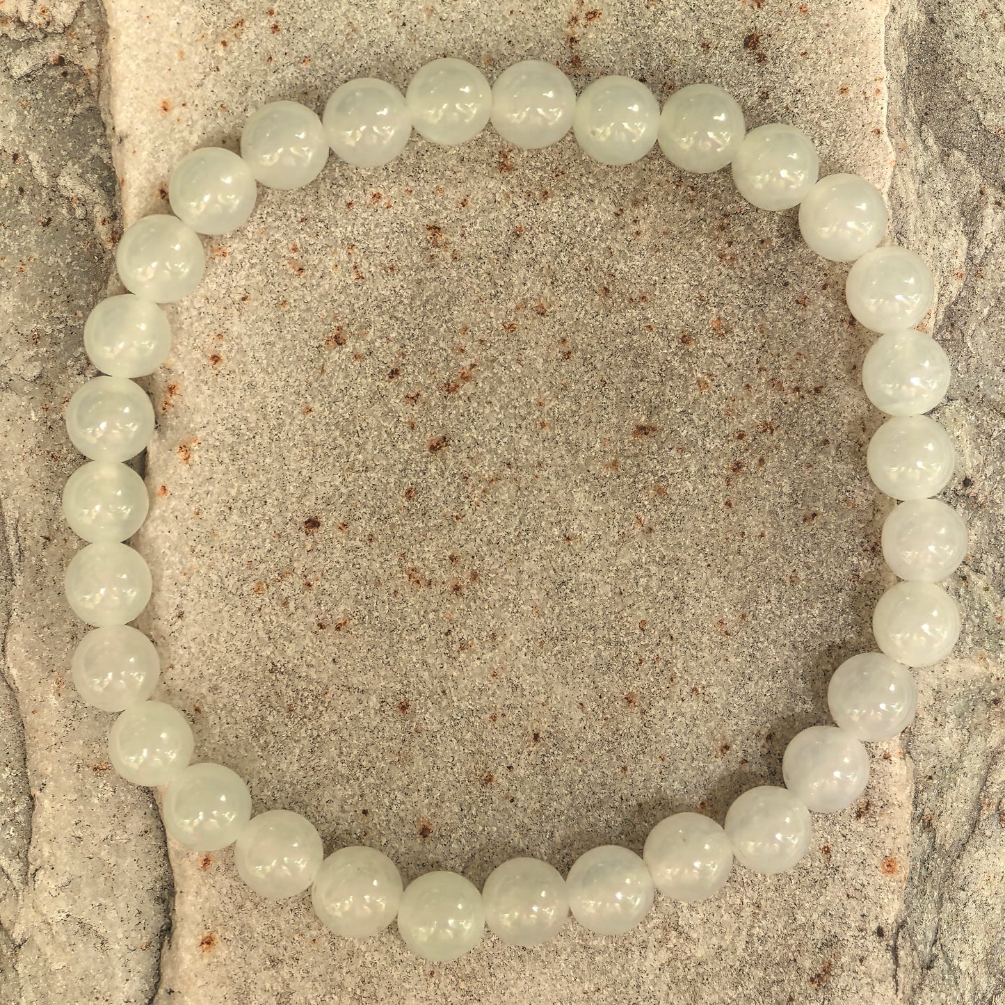 White jadeite beaded bracelet arranged in a full circle on stone surface.
