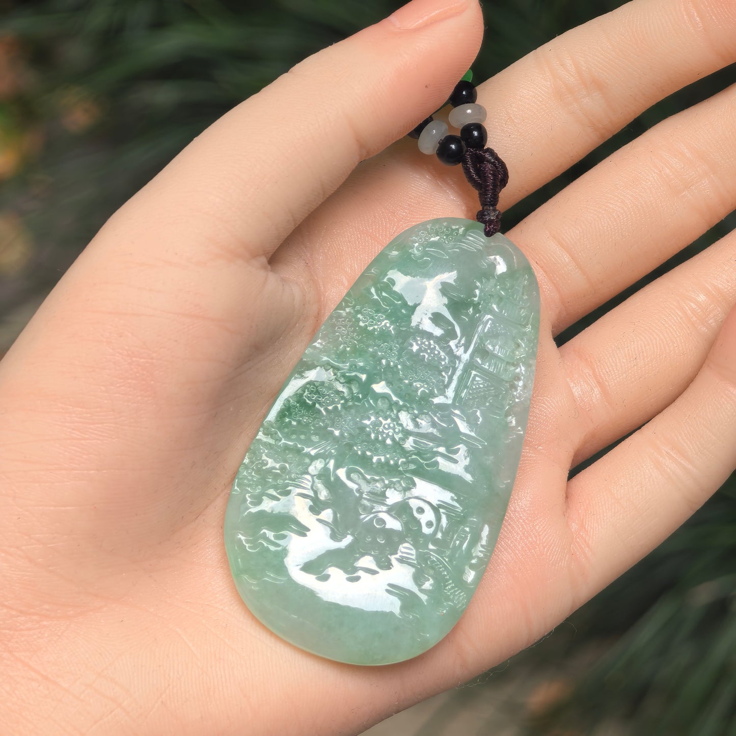 Close-up of a large green jadeite pendant with detailed mountain-and-water carving.
