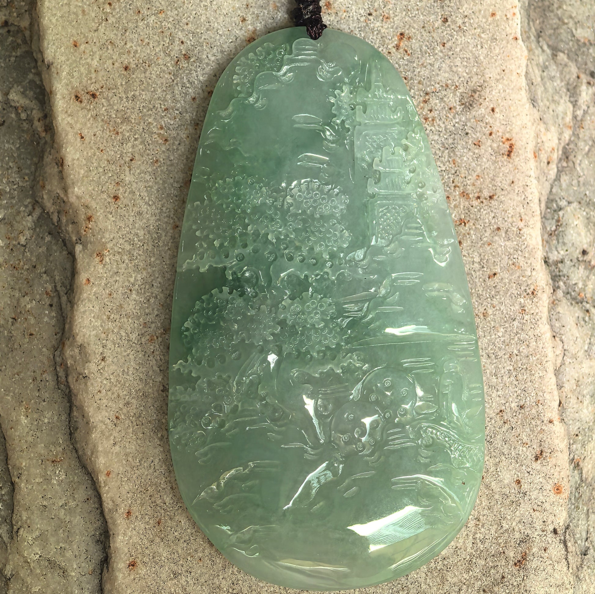 Carved jadeite landscape pendant showing trees, architecture, and flowing scenery.
