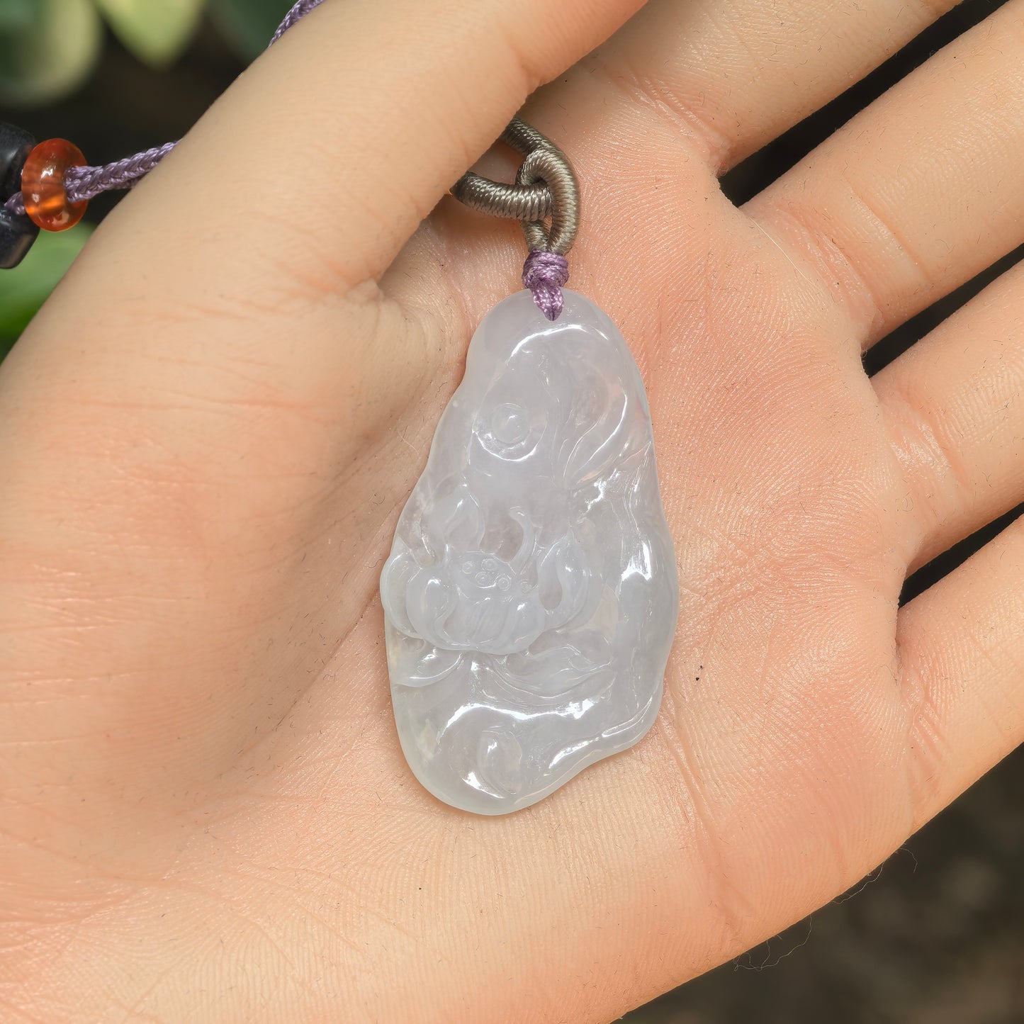 Handheld white jadeite lotus pendant with carved petals and irregular plaque form.
