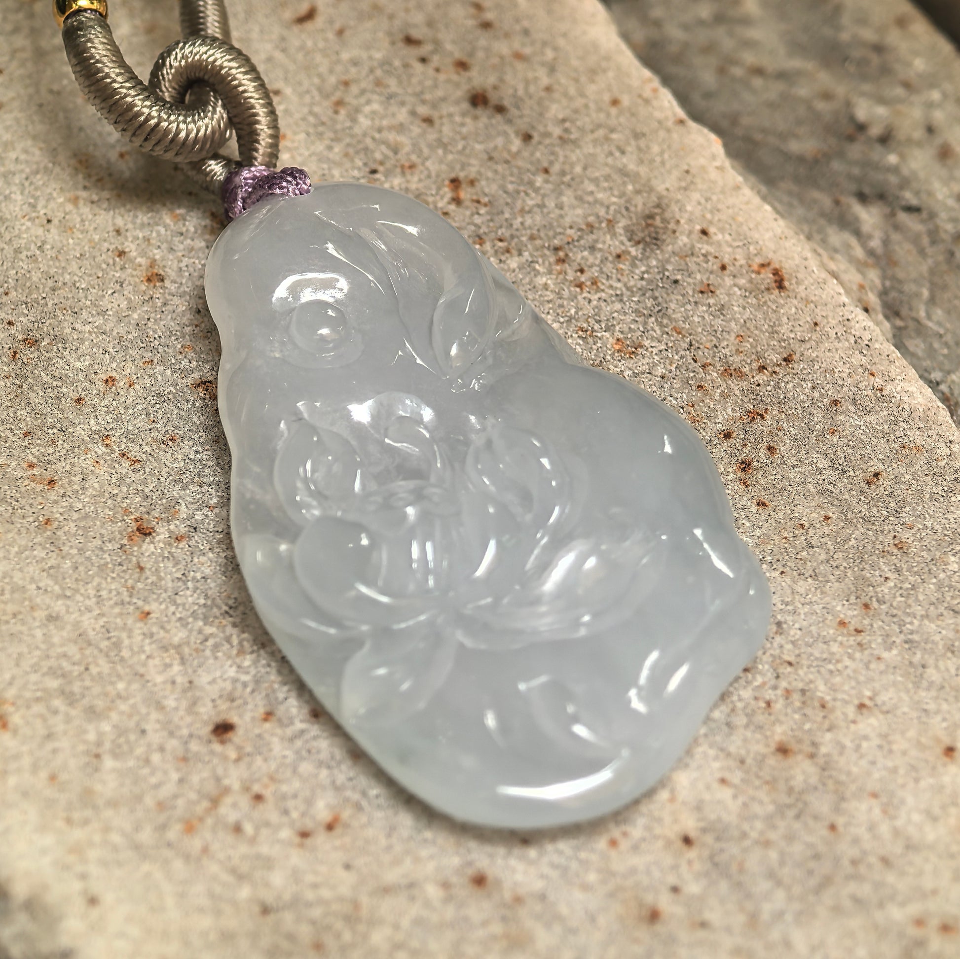 Detailed view of carved lotus jadeite pendant showing raised flower design and polished surface.
