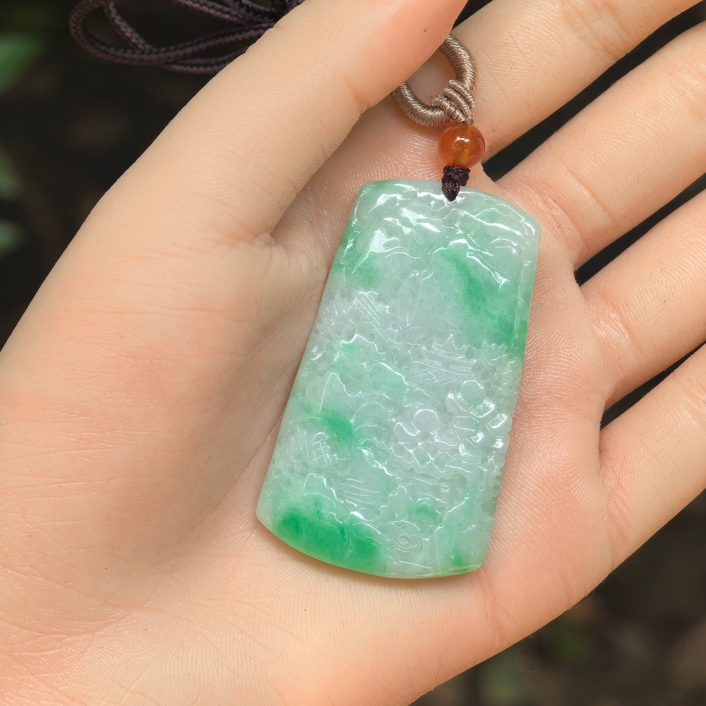 Close-up of a light green jadeite plaque pendant with detailed landscape carving.
