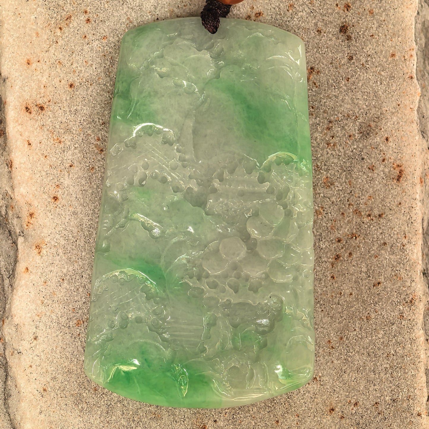 Large jadeite landscape pendant showing trees, architecture, and mountain-water scenery.
