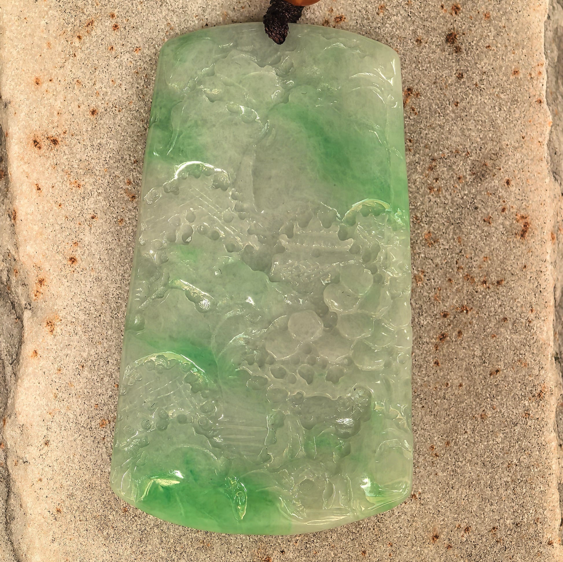 Large jadeite landscape pendant showing trees, architecture, and mountain-water scenery.
