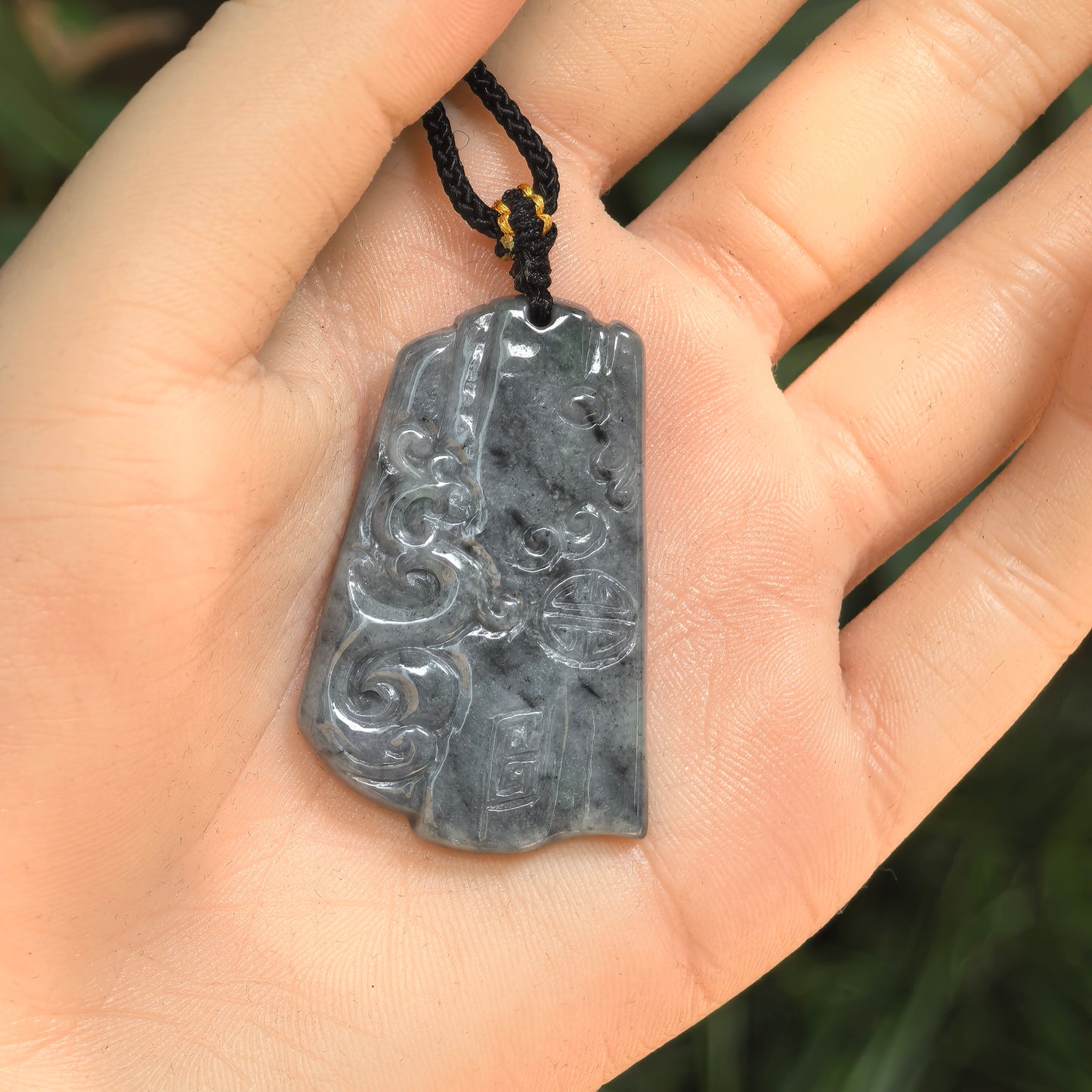 Handheld gray-black jadeite phoenix pendant showing relief carving and polished surface.
