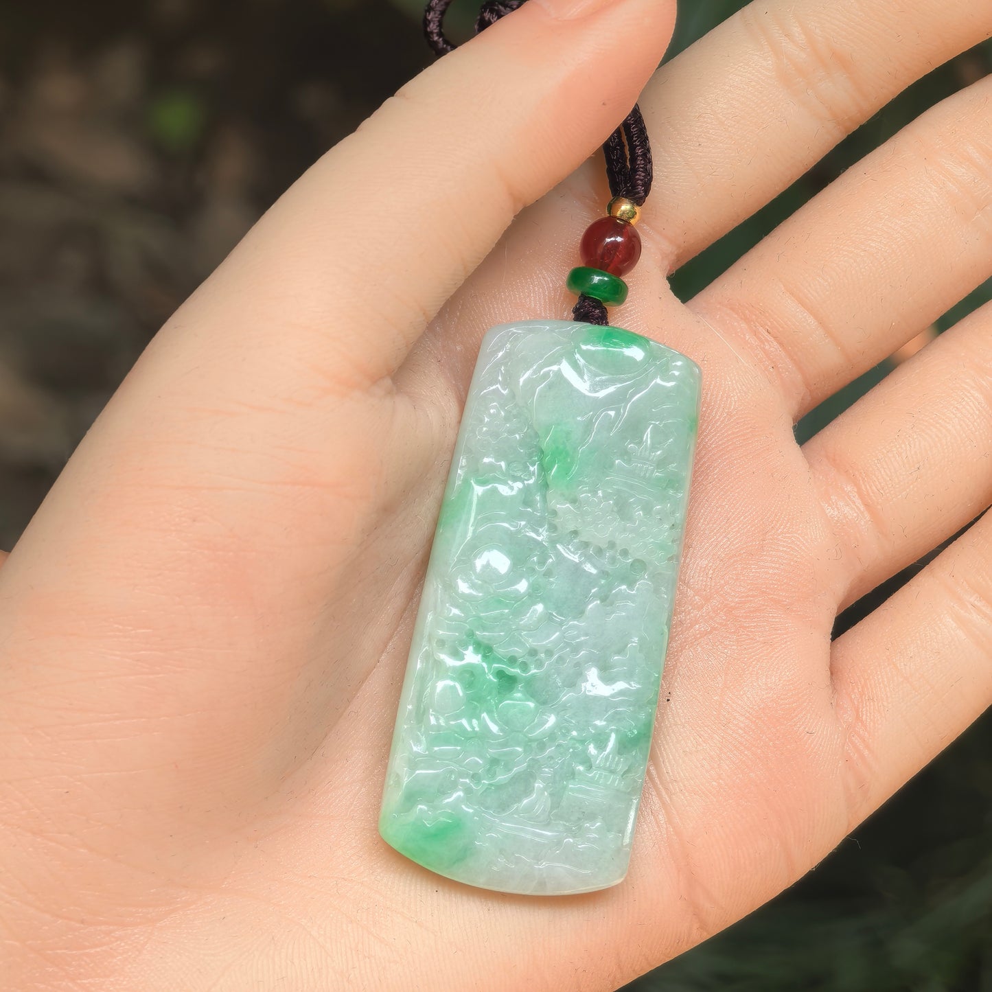 Close-up of a light green jadeite plaque pendant with detailed landscape carving.