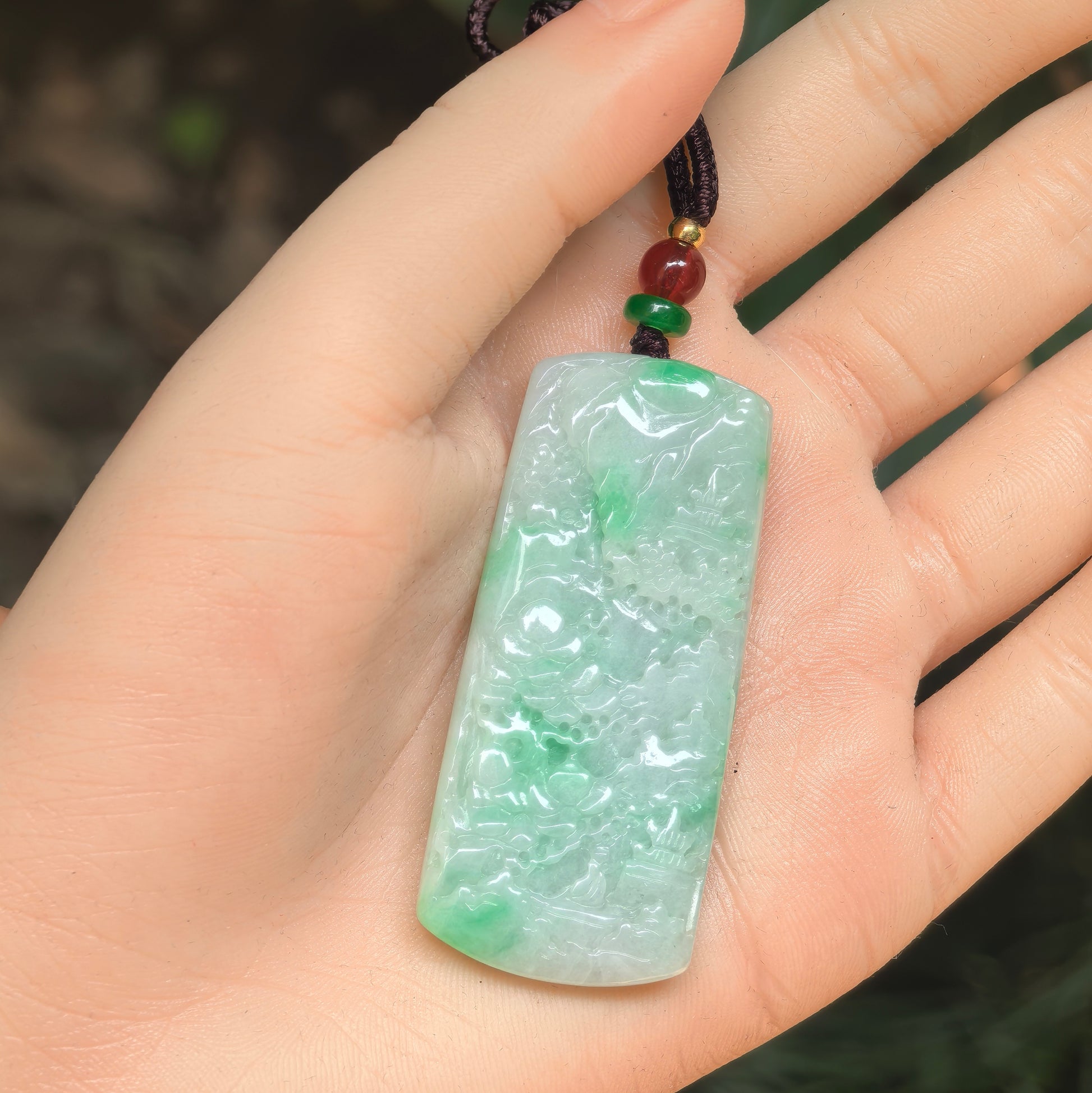 Close-up of a light green jadeite plaque pendant with detailed landscape carving.