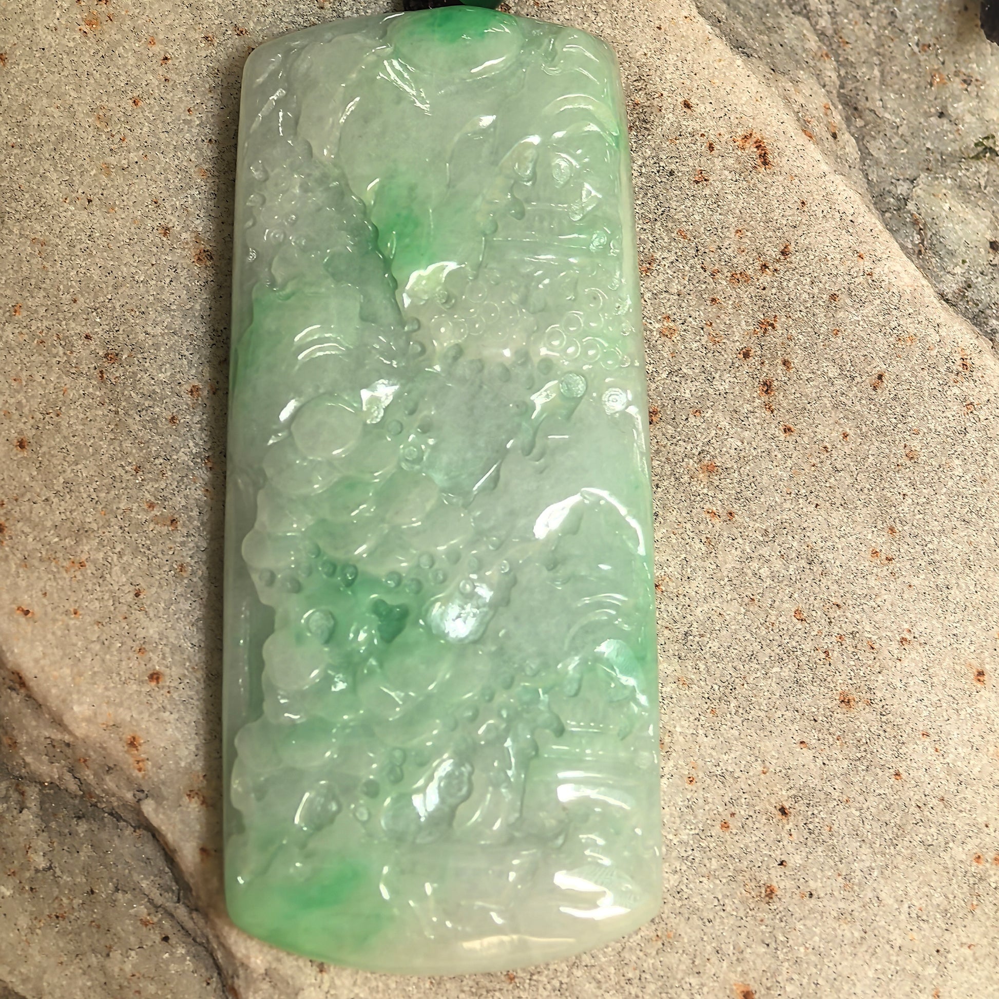 Large jadeite landscape pendant showing trees, architecture, and mountain-water scenery.
