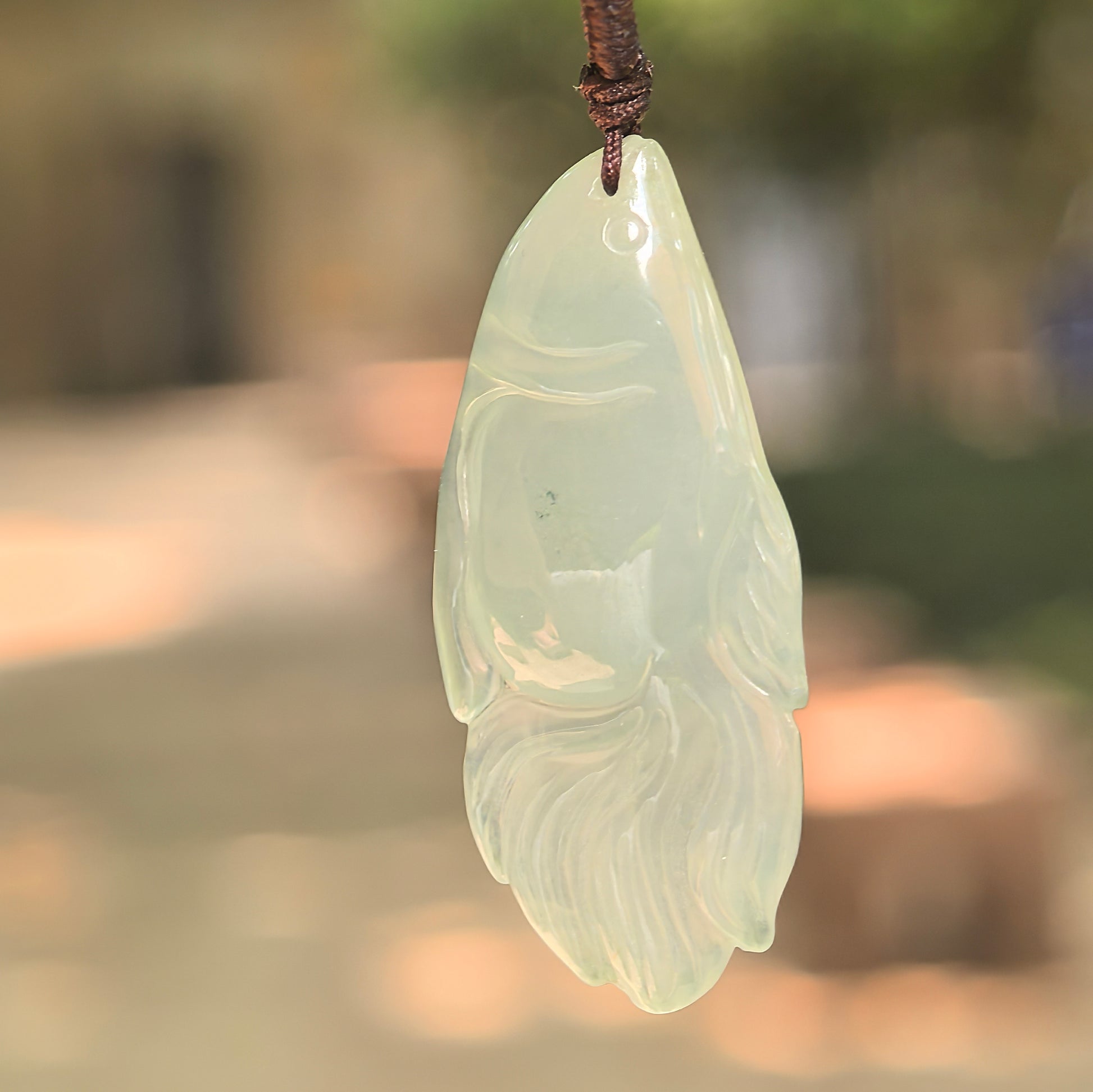 Natural Grade-A icy light green fish jadeite pendant hanging on cord in natural light.

