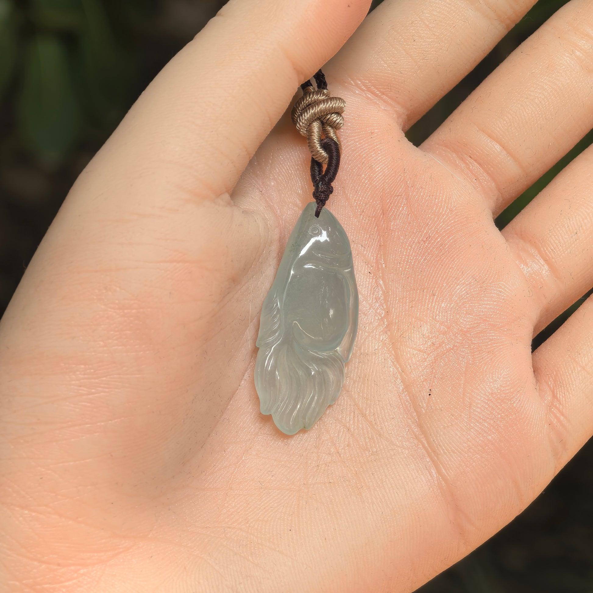 Handheld light green fish jadeite pendant showing its small size and polished icy texture.

