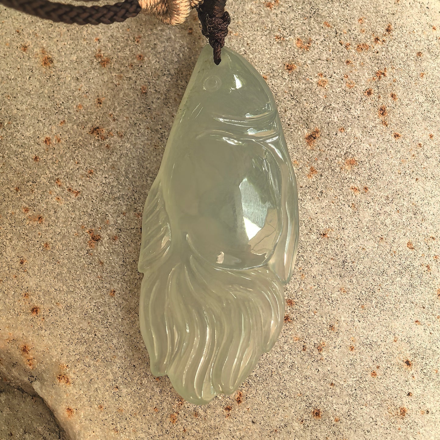 Close-up of carved fish jadeite pendant with rounded body, fins, and detailed tail design.
