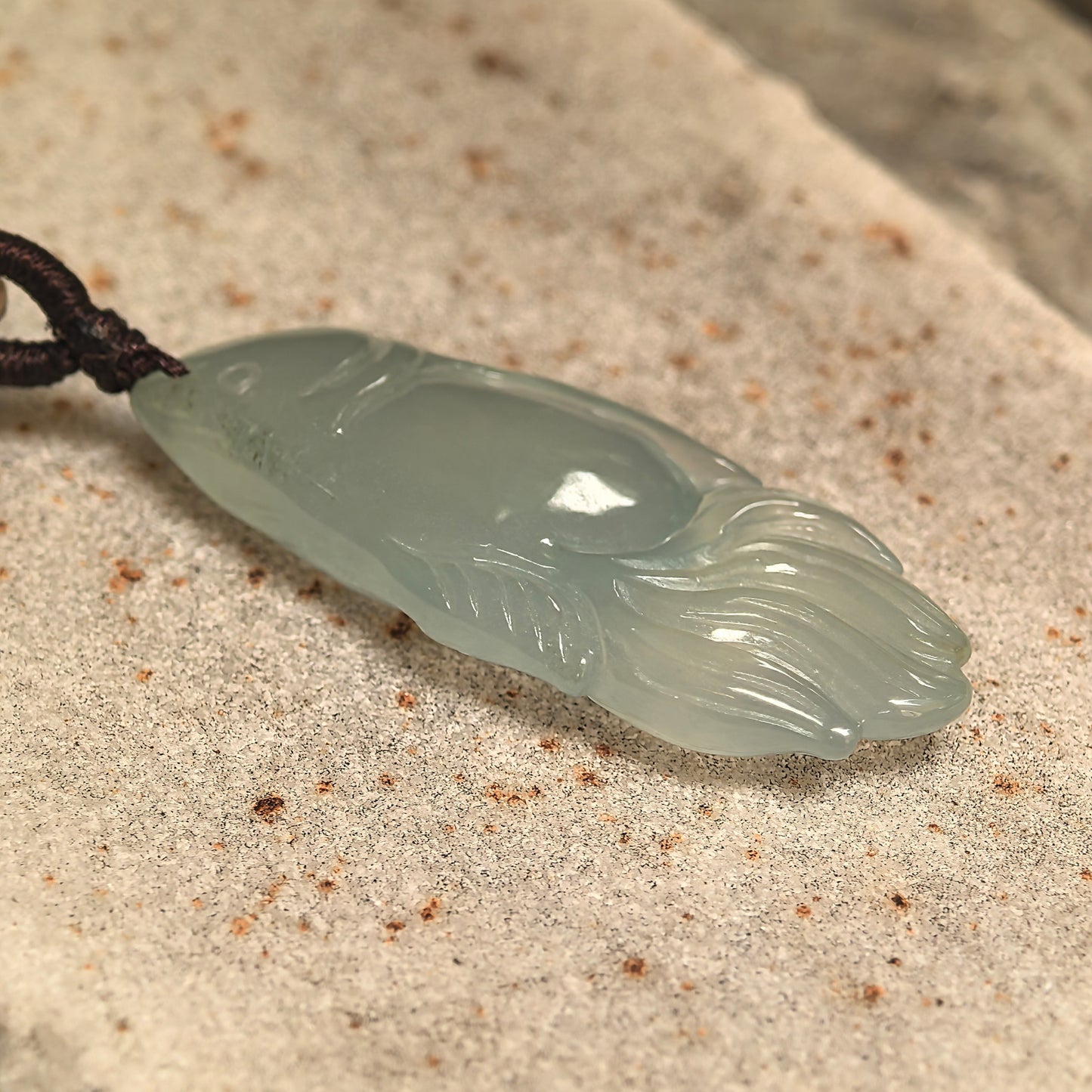 Side view of light green icy jadeite fish pendant showing thickness and smooth carving.

