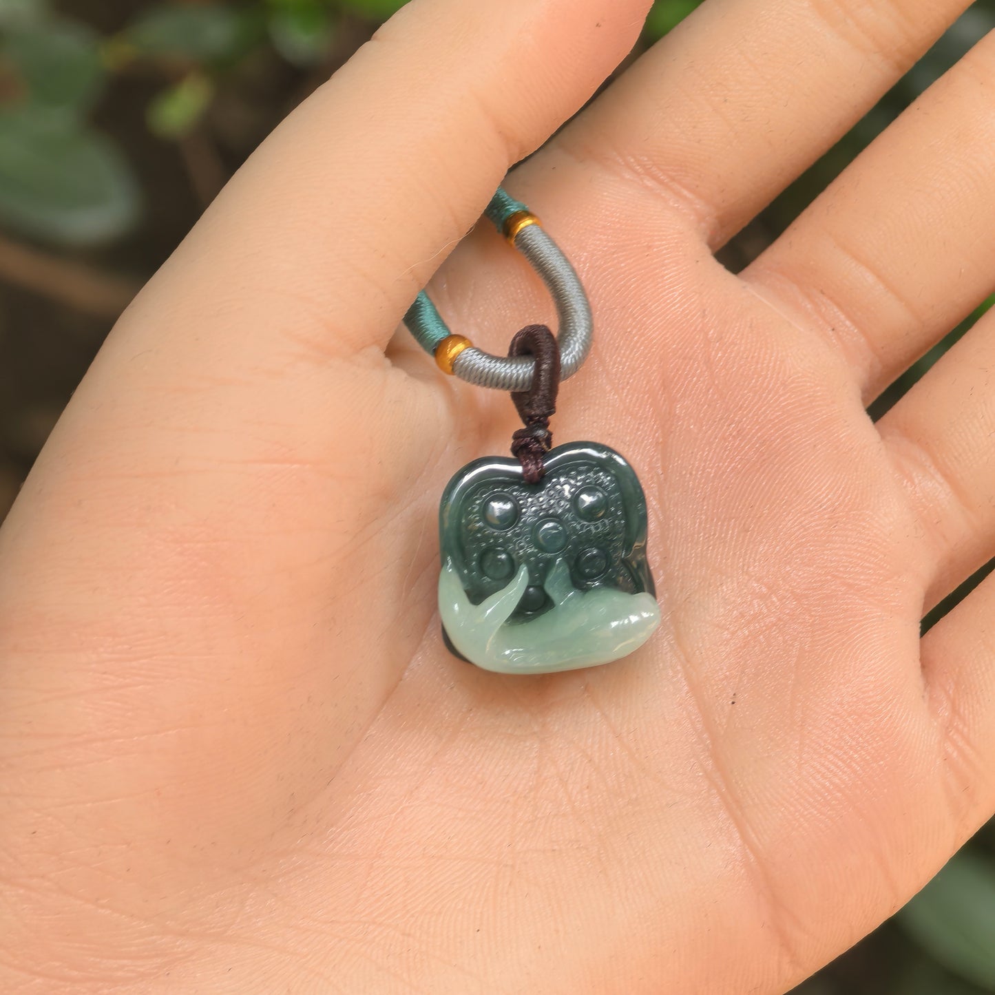 Handheld two-tone jadeite pendant showing compact fish and lotus seed carving.
